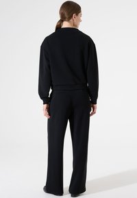 Sudadera negra de corte relajado con puños acanalados, combinada con pantalones anchos a juego. Textura de tela suave y detalles mínimos.