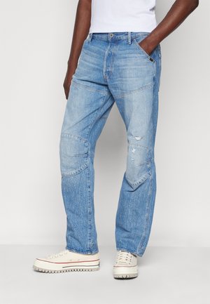 Light blue denim jeans with a loose fit, features include patchwork detailing, visible stitching, and distressed accents near the knees.