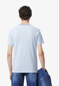 T-shirt azzurro chiaro a maniche corte con scollo a girocollo e finiture a contrasto. Tessuto di cotone liscio; abbinato a jeans in denim blu e a una giacca.