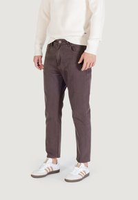 Pantalones de algodón marrones con un corte recto, diseño de cinco bolsillos y detalles de costura visibles, combinados con zapatillas blancas y un suéter crema.