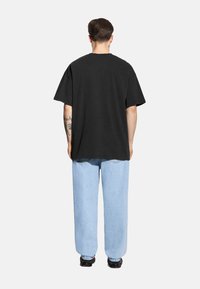 Czarny bawełniany t-shirt o luźnym kroju, z krótkimi rękawami i prostym dołem, zestawiony z jasnoniebieskimi, luźnymi dżinsami.