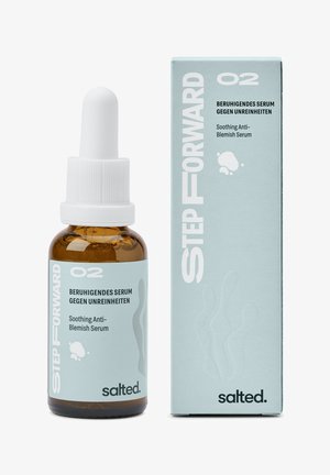 Brun glasdråberflaske med et hvidt låg, mærket "Lindrende Anti-Ufuldkommenheds Serum", ved siden af en lyseblå æske med abstrakte mønstre.