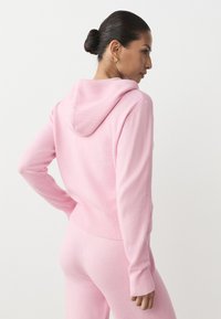 Różowa dzianinowa bluza z kapturem z prążkowanymi detalami, kapturem ze sznurkiem, dopasowanymi rękawami i luźnym krojem. Miękka faktura i bezszwowy tył.