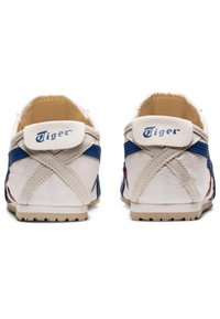Scarpe di tela bianche con accenti blu e rossi, caratterizzate da una superficie texturizzata, design a cuciture incrociate e un'etichetta con il marchio sul tallone.