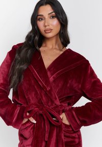 Burgundy mjuk morgonrock med sjalkrage, knytbälte och framfickor. Har en slät yta och långa ärmar med kontrasterande kant.