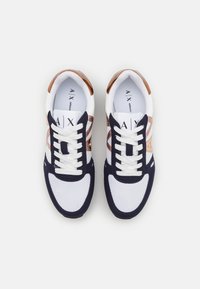 Sneakers featuring a mix of white mesh, navy suede, and metallic bronze accents. Rounded toe, lace-up design, and logo detail on the tongue.
