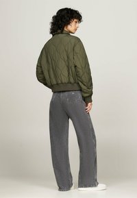 Chaqueta bomber acolchada verde oliva con puños y bajo de canalé, combinada con jeans de pierna ancha gris y zapatillas blancas.