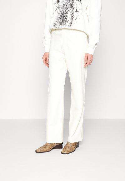 Λευκά παντελόνια με φαρδιά γραμμή από λεία ύφασμα, συνδυασμένα με καφέ μποτάκια με σχέδιο φίδι και χαμηλό τετράγωνο τακούνι.