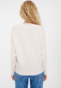 Lichtbeige geribde trui met lange mouwen, ronde halslijn en een ontspannen pasvorm. Gecombineerd met blauwe denim jeans.
