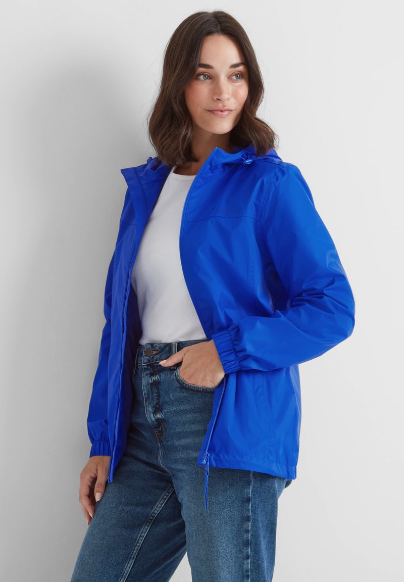 Blue lightweight jacket with a hood, elastic cuffs, and a front zipper. Worn over a white shirt, paired with blue jeans. Smooth texture.