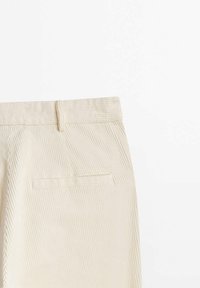 Pantalon en velours côtelé beige montrant la zone arrière de la taille avec une passants de ceinture et une poche à fente simple sur fond blanc.