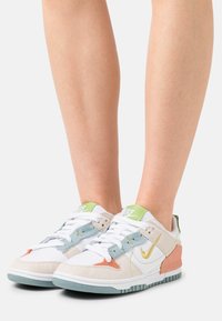 Nike-sneakers har en vit meshtopp med mjuk grå mocka, ljusblå accenter, korallfärgad sidopanel och mintgrön häl. Vita snören fulländar utseendet.