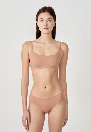 Set di reggiseno e slip in un morbido tessuto di colore marrone chiaro, senza cuciture. Il reggiseno presenta spalline sottili e una fascia semplice, mentre gli slip hanno un taglio a vita bassa.