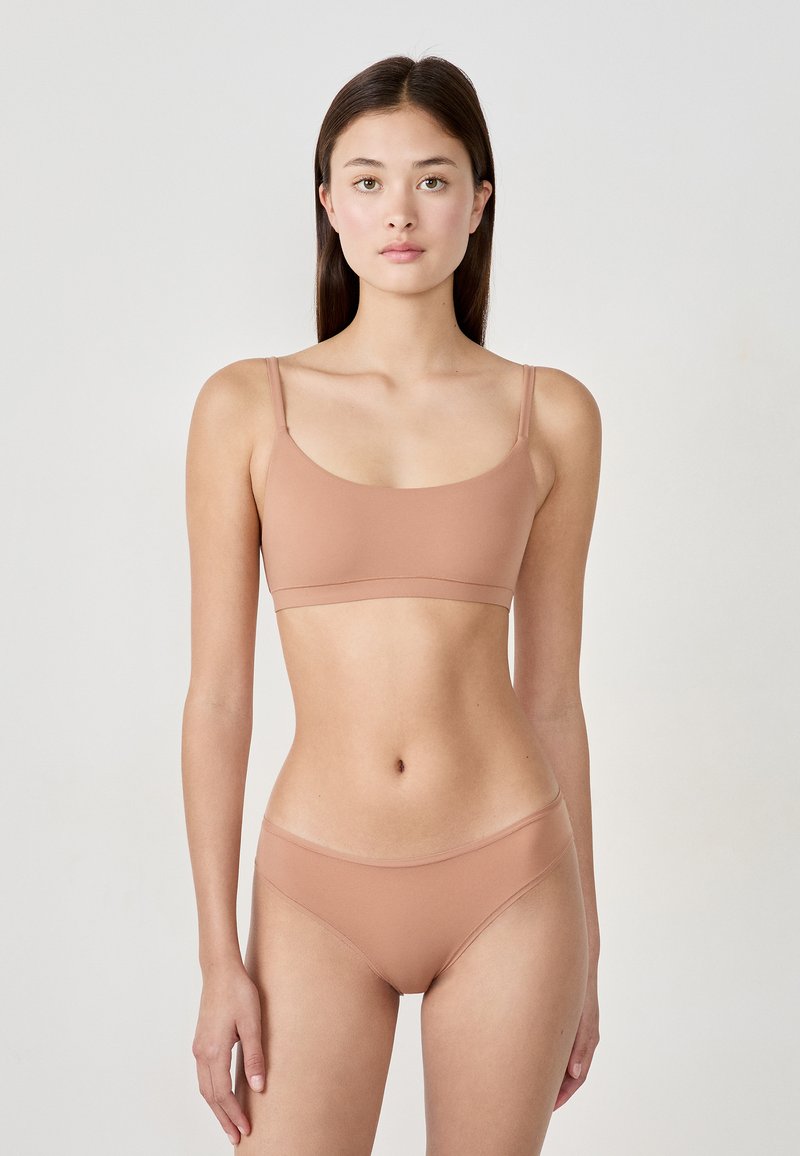 Set di reggiseno e slip in un morbido tessuto di colore marrone chiaro, senza cuciture. Il reggiseno presenta spalline sottili e una fascia semplice, mentre gli slip hanno un taglio a vita bassa.