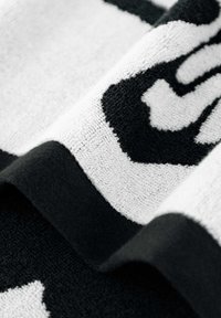 Ręcznik w czarno-białe wzory o fakturowanej powierzchni, z wyrazistymi wzorami i kontrastującą, solidną czarną bordiura wzdłuż krawędzi.