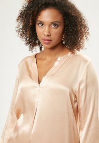 Helles rosa Satinbluse mit V-Ausschnitt, langen Ärmeln und einem subtilen Glanz. Verfügt über eine Frontleiste und einen entspannten Schnitt.
