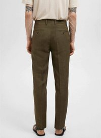 Olijfgroene broeken met een getailleerde pasvorm, voorzien van twee achterzakken en een gladde textuur, gecombineerd met een lichtgekleurde shirt en sandalen.