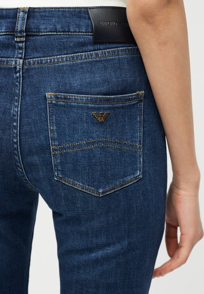 Μπλε τζιν υφασμάτινο παντελόνι με εμφανή πίσω τσέπη που διαθέτει μικρό μεταλλικό λογότυπο Emporio Armani και μαύρο δερμάτινο σήμα της μάρκας.