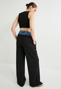 Pantaloni neri a vita alta con un accento in denim sulla vita, design a gamba larga e tasche. Top corto nero a costine visto da dietro.