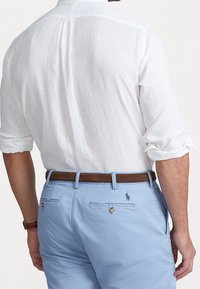 Vit lin skjorta, blå shorts med bakfickor, brun läderbälte. Shorts har broderad logotyp och knappdekorationer.