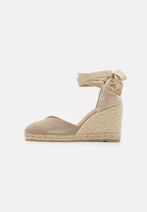 Espadrille beige à semelle compensée avec talon enveloppé de jute, bout fermé, contrefort tissé et fermeture à nouer autour de la cheville.