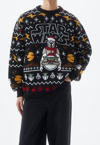 Schwarzer und mehrfarbiger gestrickter Pullover mit einem "Star Wars"-Design, das Charaktere, Schneeflocken und Muster zeigt. Gerippte Bündchen und Hals.
