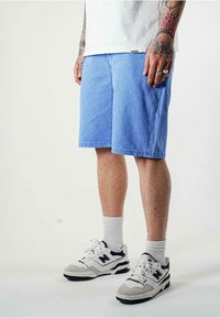Shorts in denim blu con vestibilità rilassata, dotati di tasche laterali. Abbinati a calze bianche e sneakers grigie con dettagli neri.