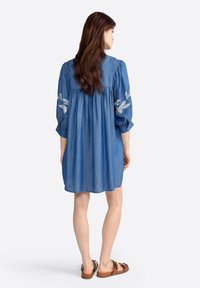 Abito in denim con maniche a tre quarti, caratterizzato da motivi di foglie ricamati sulle maniche e una vestibilità ampia che inizia dal corpetto.