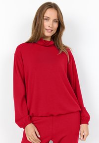 Red pullover with long sleeves and a draped cowl neck. Made of soft, smooth fabric. Features elastic cuffs and a relaxed fit.