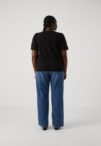 Black crochet top with short sleeves, featuring a textured pattern. Paired with loose blue denim jeans. View from the back.