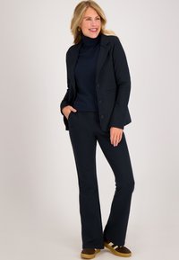 Marineblauwe blazer met twee knopen en zijzakken, gecombineerd met een marineblauwe coltrui en bijpassende bootcutbroek. Zacht materiaal, relaxte fit.