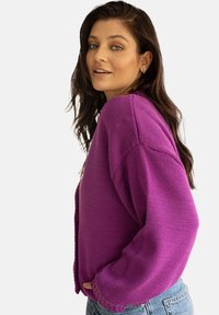 Fioletowy sweter z dzianiny z długimi rękawami i teksturowanym materiałem. Luźny krój z prążkowanym dołem i mankietami, w połączeniu z niebieskimi dżinsami.