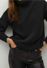 Czarny dzianinowy sweter z golfem, z prążkowanymi mankietami i dołem, noszony na wysokim stanem spodniach z czarnej sztucznej skóry. Widoczne teksturowane detale tkaniny.