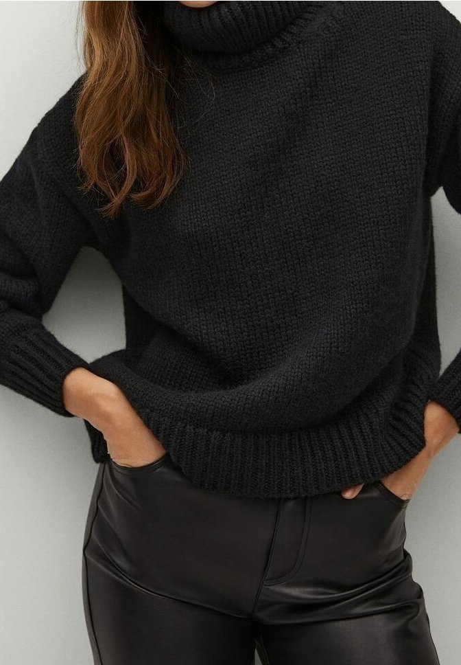 Czarny dzianinowy sweter z golfem, z prążkowanymi mankietami i dołem, noszony na wysokim stanem spodniach z czarnej sztucznej skóry. Widoczne teksturowane detale tkaniny.