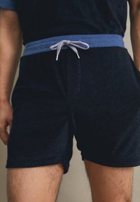 Shorts bleu marine en tissu éponge doux, avec un cordon de serrage bleu clair et une taille élastique, comportant des poches latérales et une coupe décontractée.