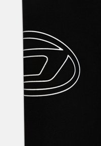 Melnā audumam ar gludu tekstūru ir izteikts balts logos, kas sastāv no stilizēta ovāla un ģeometriskām formām.