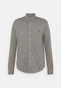 Camisa de botón de manga larga gris en una tela suave y texturizada. Presenta un cuello clásico y un pequeño logo en el lado izquierdo del pecho.