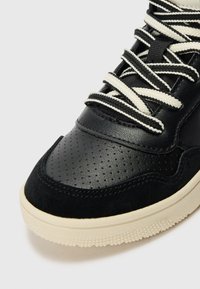 Baskets noires avec une tige en cuir texturé et perforations, accents en suède, et des lacets et une semelle de couleur crème. Design à bout rond.