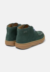 Botas de tobillo de ante verde con suela marrón, que presentan un sutil logo de Camper y cordones claros, vistas desde la parte posterior.