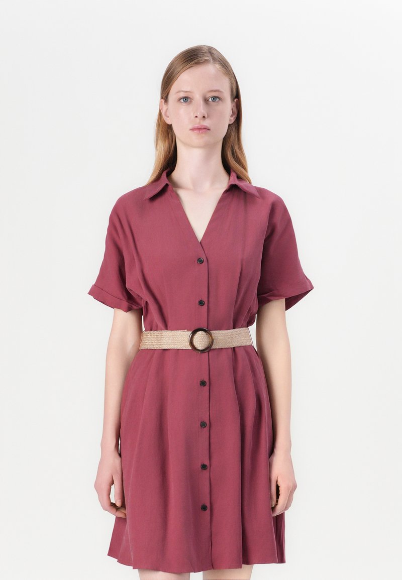 Robe boutonnée bourgogne à manches courtes et décolleté en V. Elle présente une ceinture tissée avec une boucle ronde, un tissu lisse et une silhouette fluide.