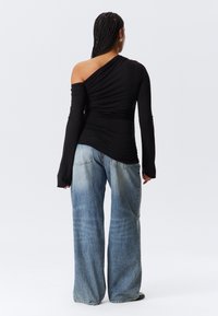 Top nero a spalla unica con texture arricciata, abbinato a jeans in denim azzurri chiari, larghi con dettagli sbiaditi.