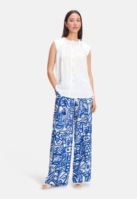 White sleeveless blouse with a ruffled neckline, paired with wide-leg pants featuring bold blue abstract patterns on a light background.