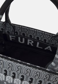 Sac Furla noir et gris avec motif monogramme, ouverture supérieure montrant l'intérieur noir et une poche zippée à l'intérieur.