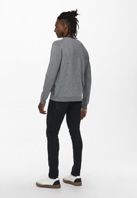 Grijze trui van zacht materiaal, met geribbelde onderkant en boorden, gecombineerd met slim-fit zwarte jeans en witte sneakers met zwarte accenten.