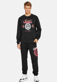 Completo felpa e pantaloni jogger neri con stampa grafica raffigurante un design di tigre, accenti bianchi e rosa, polsini a costine e tasche laterali.