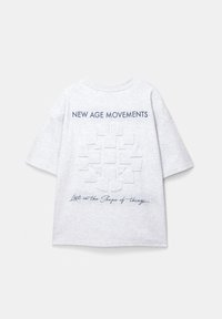 Grå T-shirt med korte ærmer, der pryder teksten "NEW AGE MOVEMENTS" og et puslespilstykke-grafik, med et håndskrevet citat nedenfor.