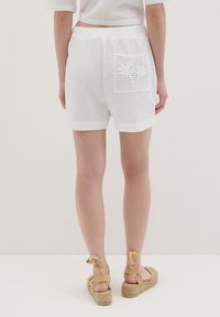 Witte shorts met elastische tailleband, voorzien van een decoratieve kantenzak. Gladde textuur met omgeslagen zoommanchetten, gecombineerd met tan espadrilles.