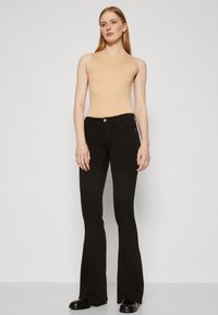 Black flared jeans with a smooth texture, featuring a front button closure and subtle side pockets, paired with a beige sleeveless top.