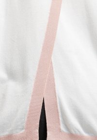 Tessuto bianco con bordi a costine rosa pallido che formano una fessura verticale sopra un indumento nero sottostante.