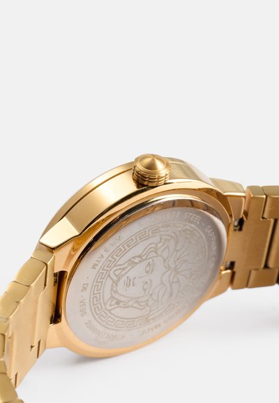 Reloj de acero inoxidable dorado con caja redonda, corona texturizada y diseño de Medusa grabado en la parte trasera. Acabado metálico brillante.
